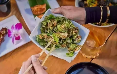 Hands at a restaurant picking up crispy green food with chopsticks.