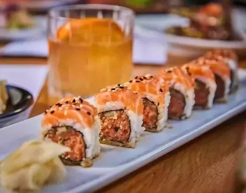 Salmon-topped sushi roll, pickled ginger, and an amber drink.
