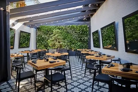 Outdoor dining area with patterned tiles, a living wall, and pergola.