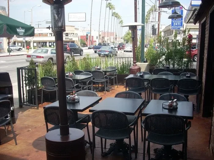 Restaurant patio with tables, heaters, and urban street with palm trees.
