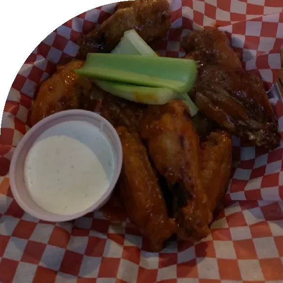 Buffalo chicken wings, celery, and dipping sauce in a basket.