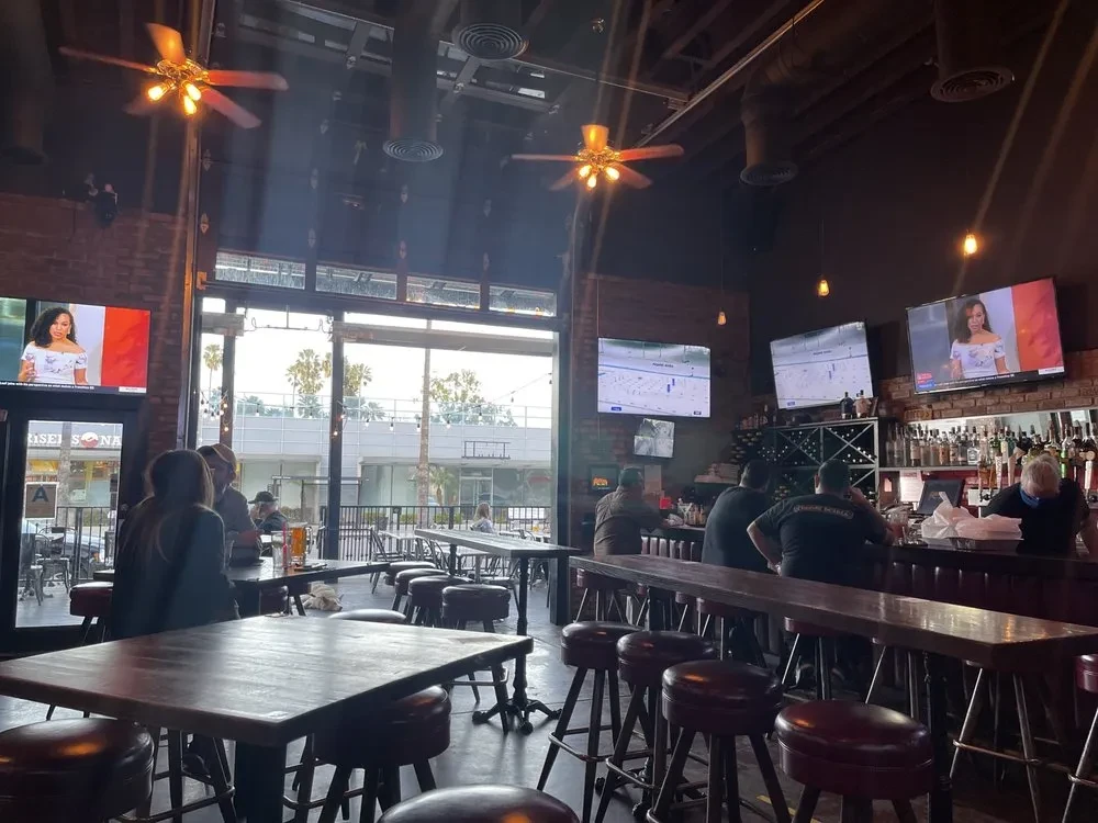 Industrial bar interior, patrons, multiple TVs, and outdoor patio view.