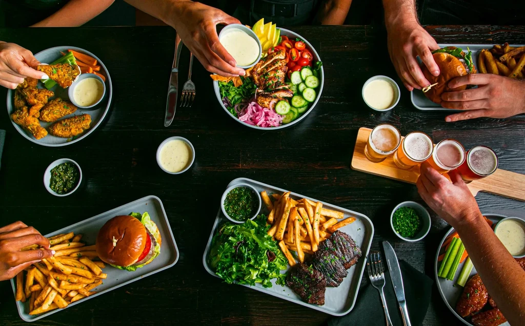 Dark wooden table laden with various dishes, beer, and active diners.