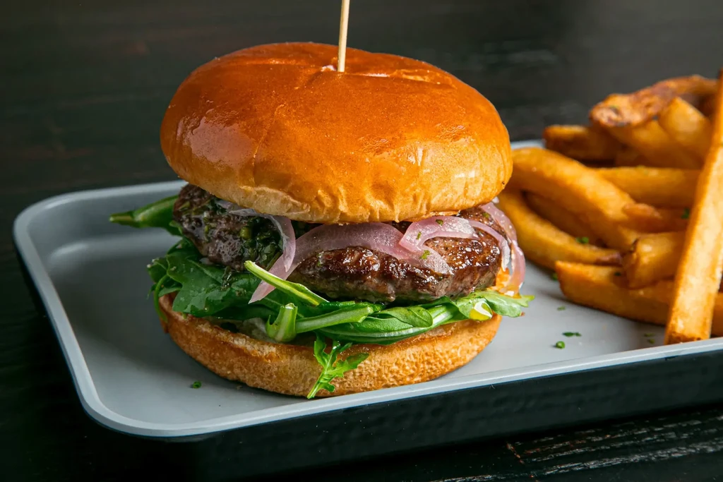 Gourmet beef burger with brioche bun, green sauce, and golden fries.