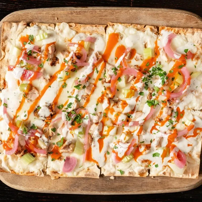 Top-down rectangular chicken flatbread with buffalo sauce, ranch, and herbs.