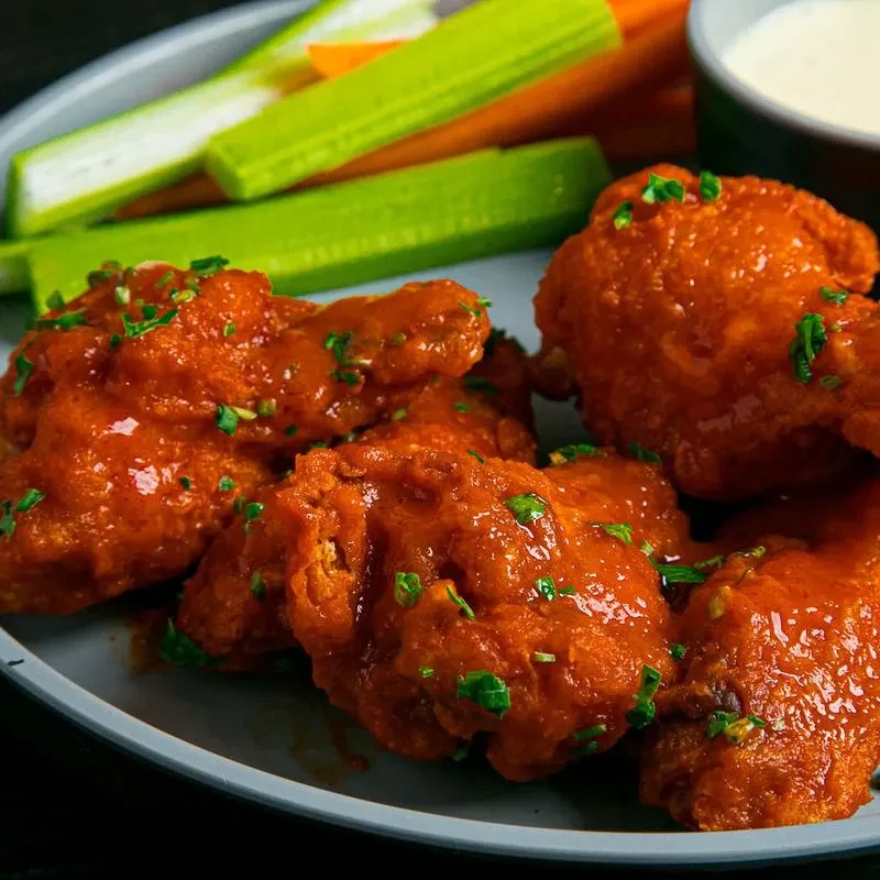 Plate of five buffalo chicken wings, celery, carrots, and dipping sauce.