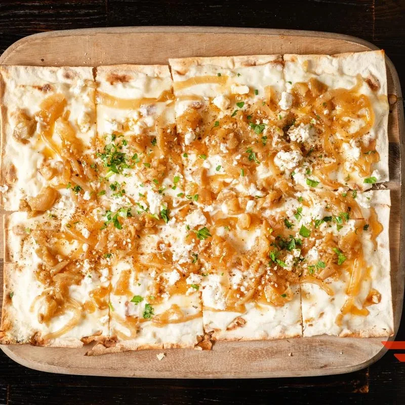 Tart flambée with caramelized onions, white cheese, herbs on a wooden board.