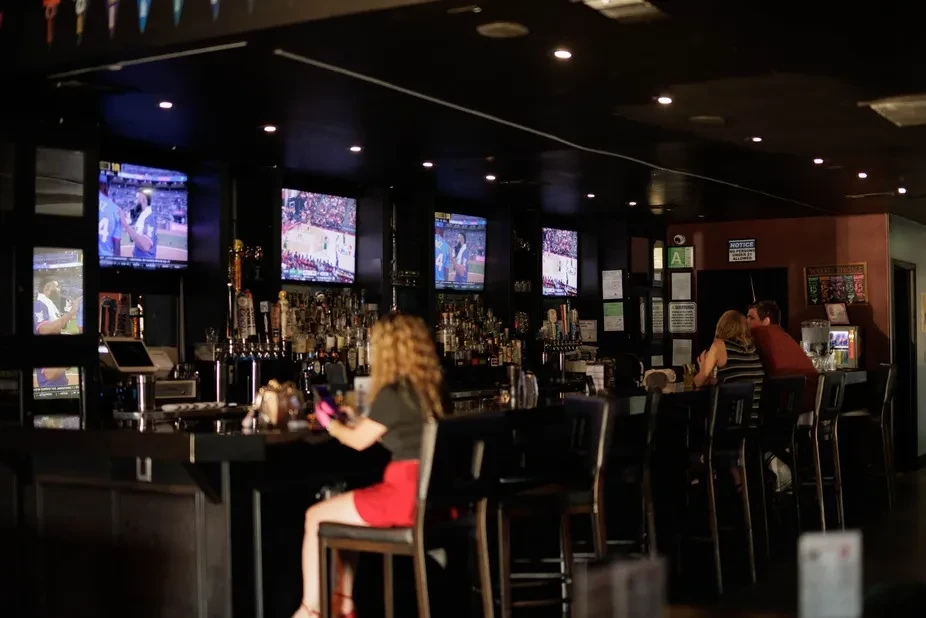 Dimly lit bar with liquor, beer taps, sports TVs, and customers.
