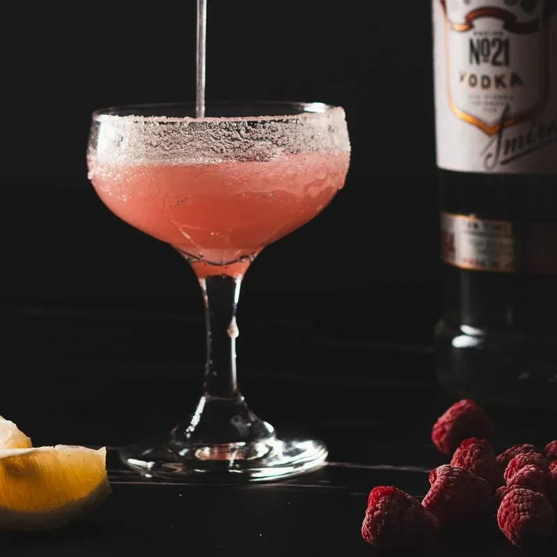 Pinkish-red cocktail poured into sugared glass with lemon, raspberries, vodka.