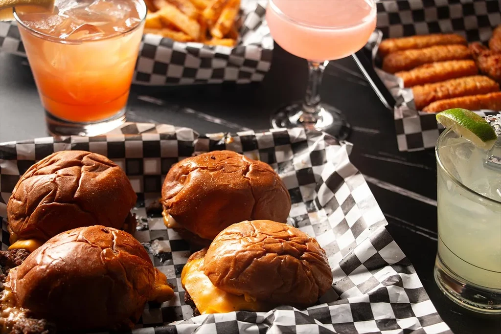 Overhead view of cheeseburger sliders, fries, cocktails, and fried snacks.