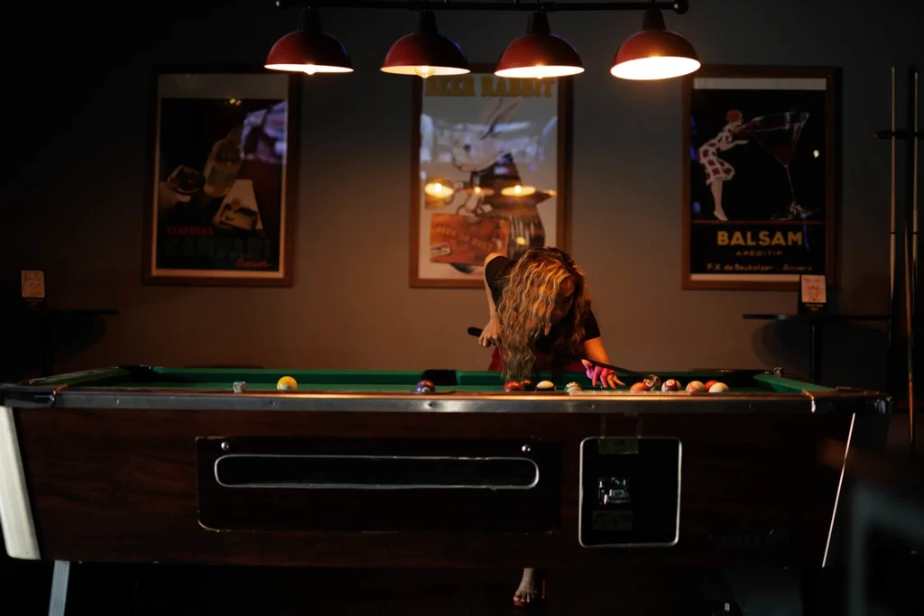 Person playing pool on a green felt table under warm lights.