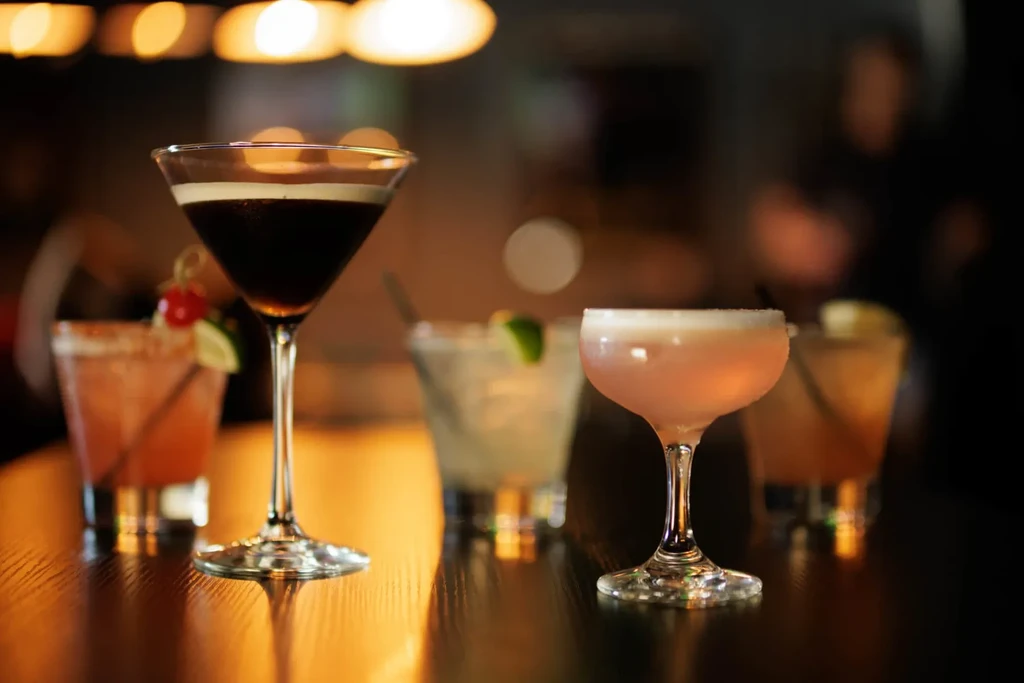 Four distinct cocktails on a dark bar, with a prominent foamy martini.
