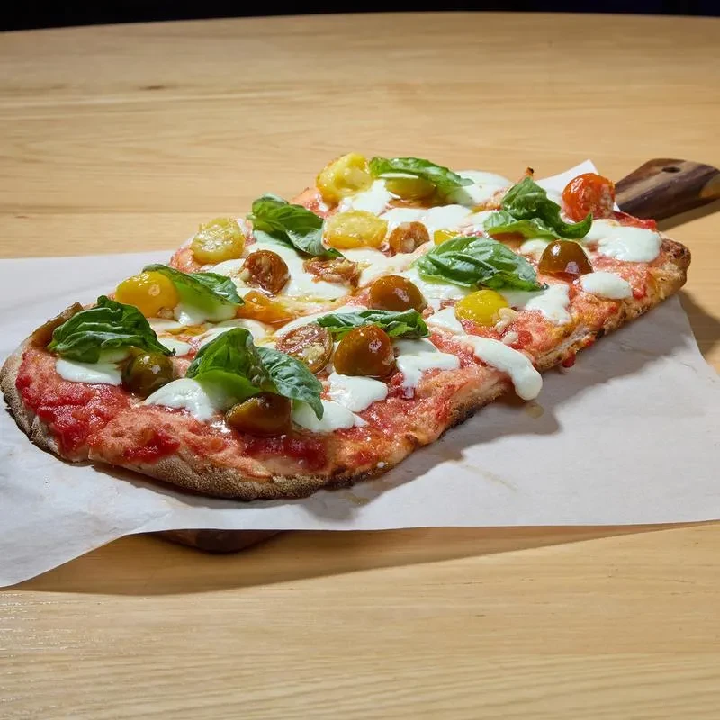 Rectangular focaccia pizza with cherry tomatoes, mozzarella, and basil on a paddle.