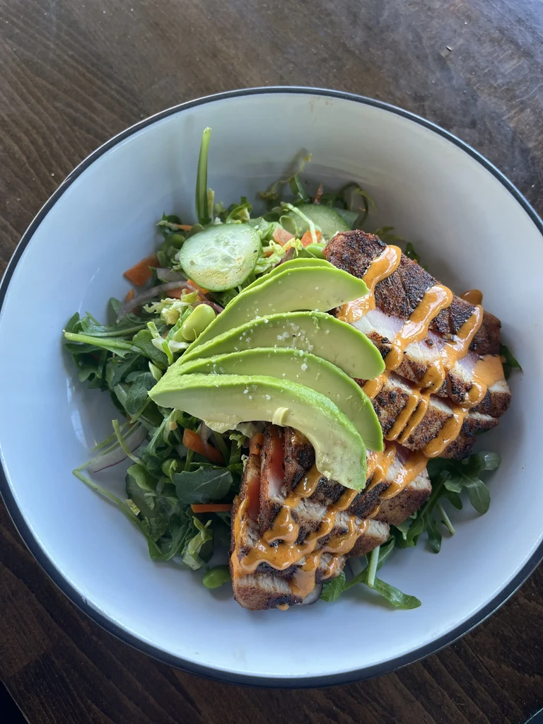 Overhead view of salad with seared protein, avocado, and creamy sauce.