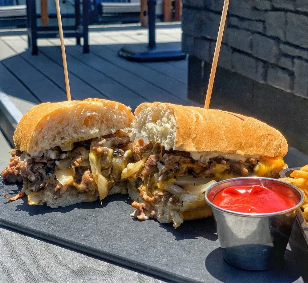 Hearty cheesesteak sandwich cut in half, served with fries and ketchup.