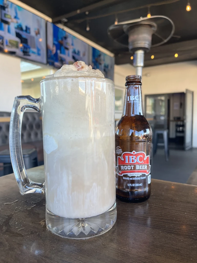 Overflowing root beer float in glass mug with IBC bottle.