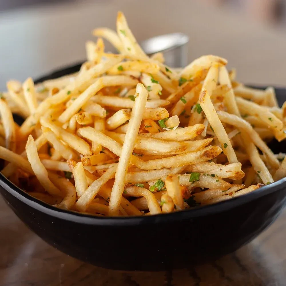 Golden brown thin-cut fries with green herbs in a dark bowl.