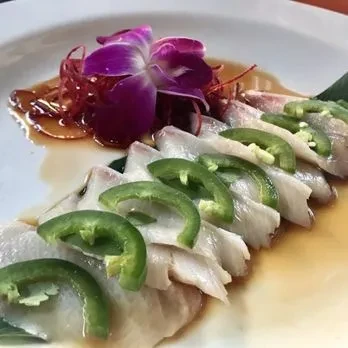 White fish sashimi with jalapeños, red threads, and purple orchid.