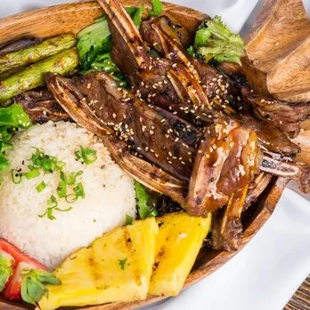 Rustic wooden bowl of grilled meat, rice, vegetables, and fruit.