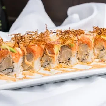 Eight sushi rolls topped with crispy shallots, fish, avocado, and orange sauce.