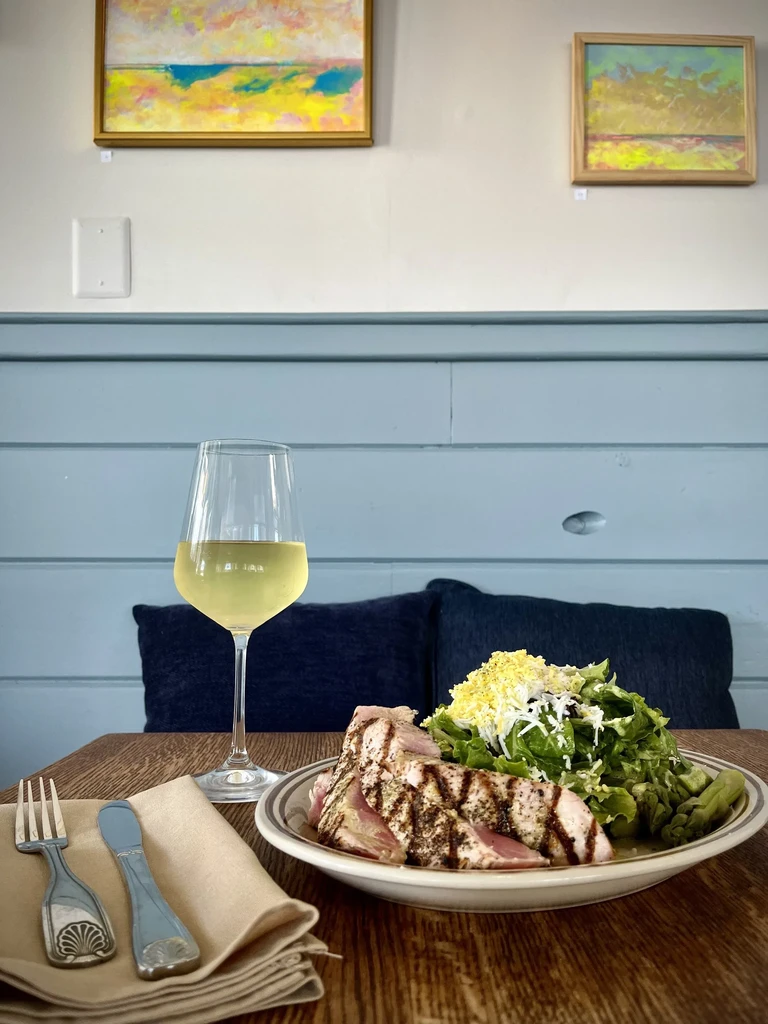 Seared tuna, green salad, and white wine on a restaurant table.
