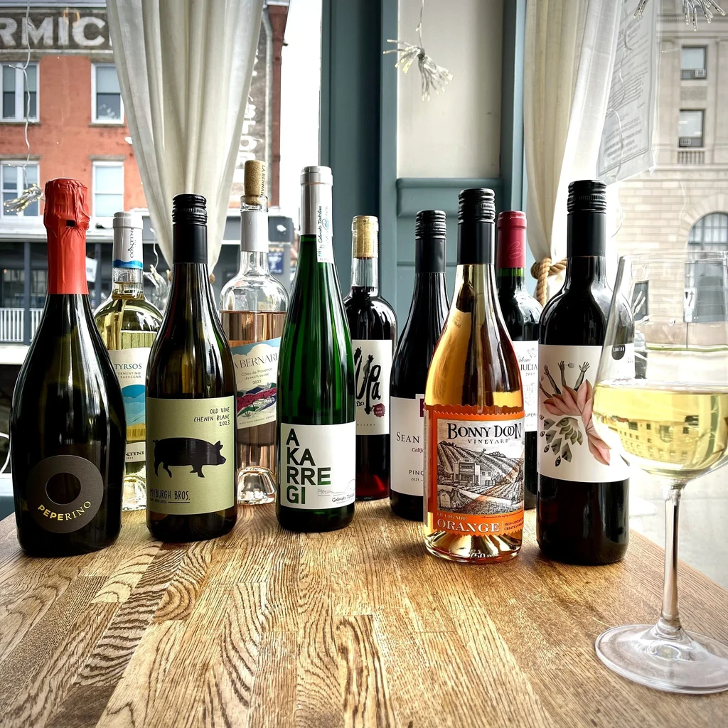 Multiple wine bottles and a filled glass on a table, city view.