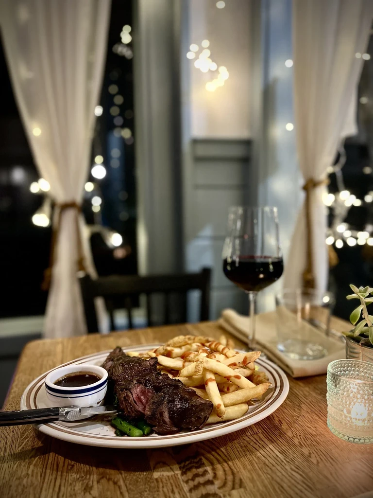 Grilled steak and french fries with red wine on a rustic table.