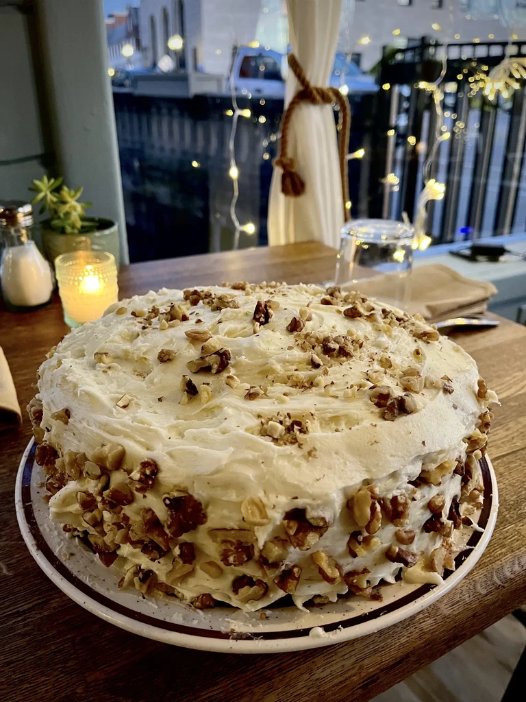 Frosted cake with walnuts, candle, and succulent on a rustic table.