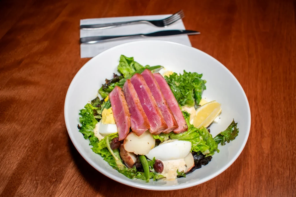 Close-up of a seared tuna Nicoise salad in a white bowl.