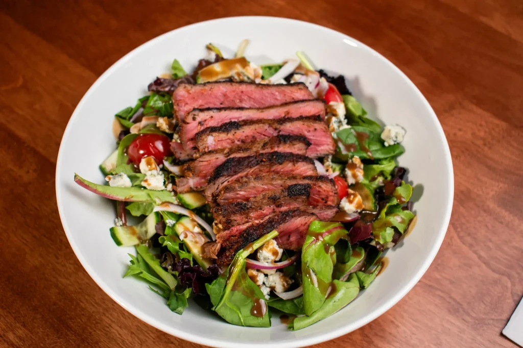 Close-up of seared steak salad with mixed greens, blue cheese, dressing.