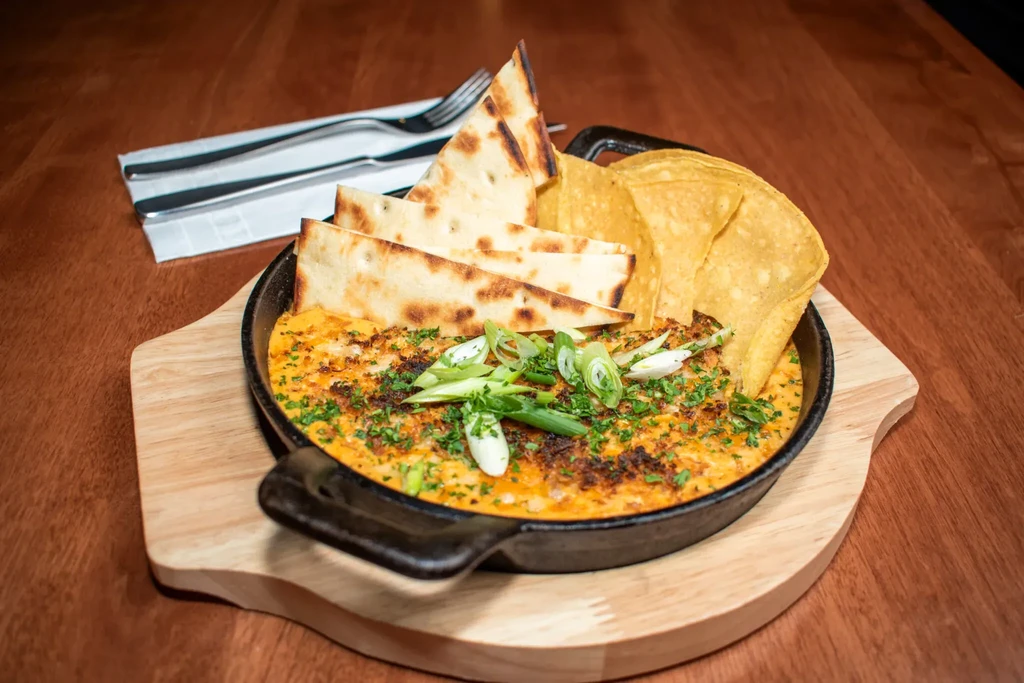 Cheesy dip in skillet, topped with green onions, flatbread, and chips.