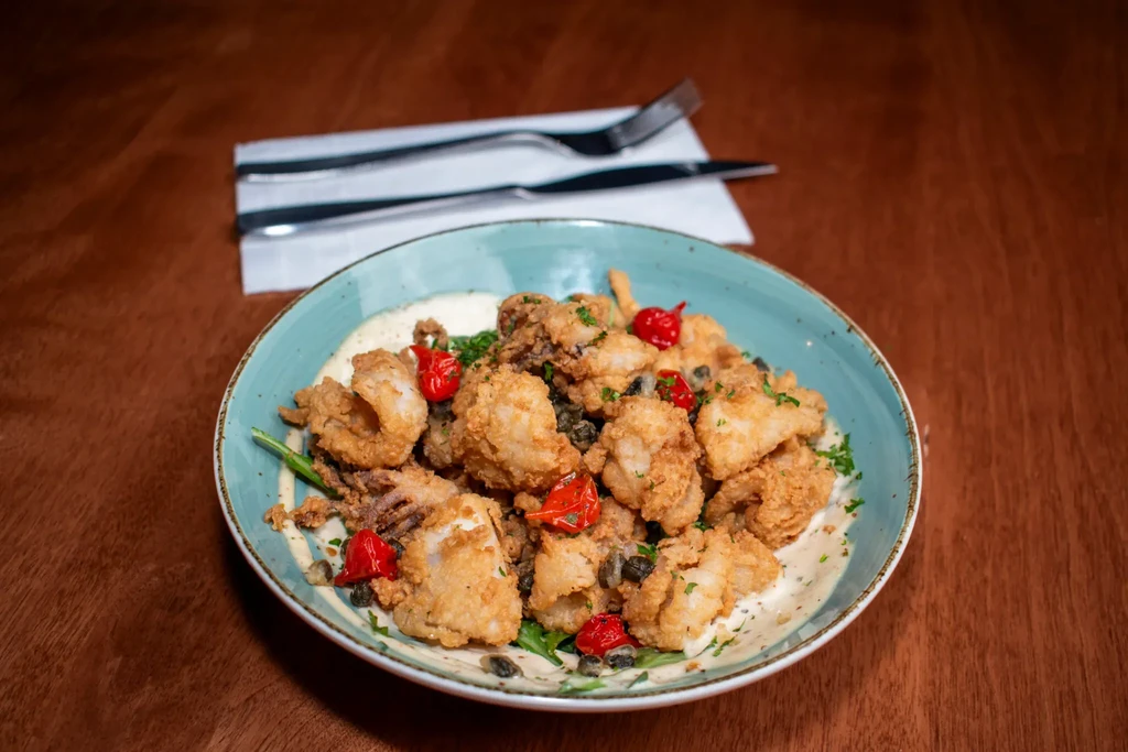 Golden calamari in a teal bowl, with peppers, capers, and parsley.