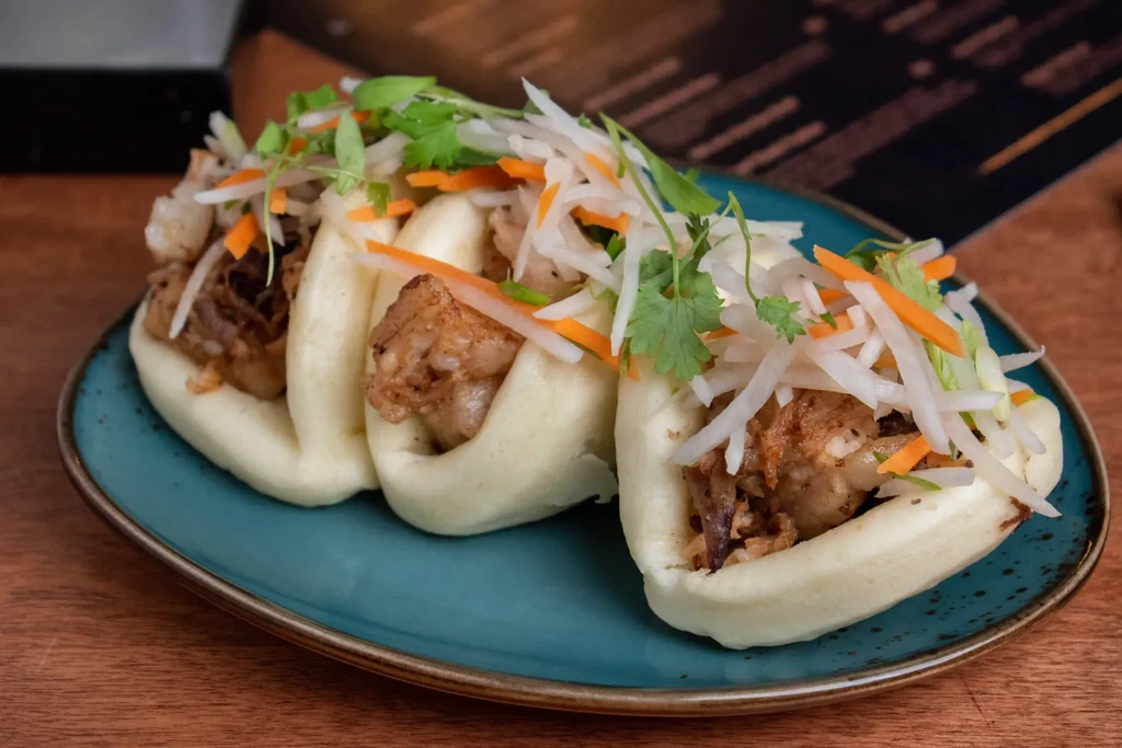Three steamed bao buns with shredded meat, radish, carrots, and cilantro.