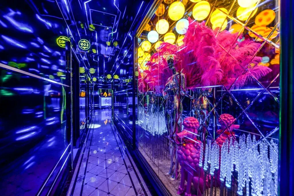 Stylized interior with neon, mirrors, mannequins, and pink poodle sculptures.
