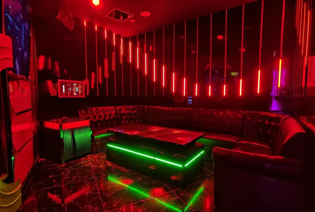 Dark, neon-lit lounge with U-shaped sofa and red-green LEDs.
