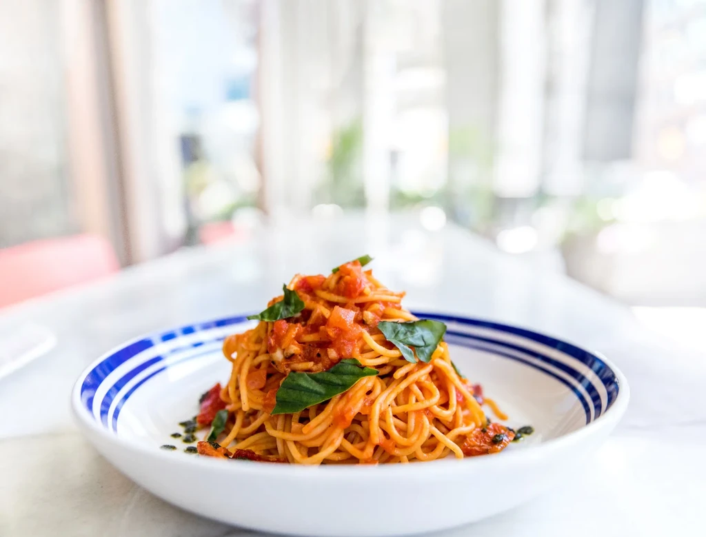 Spaghetti with chunky tomato sauce and fresh basil in striped bowl.