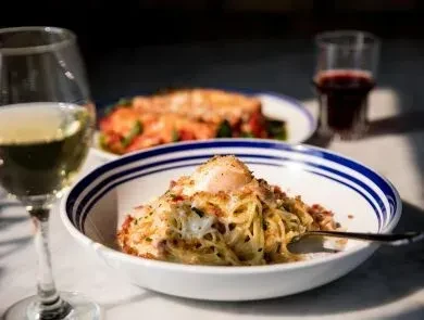 Table setting with carbonara pasta, egg yolk, and white wine.