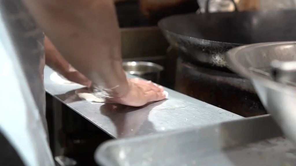 Hands kneading dough on a stainless steel counter in a professional kitchen.