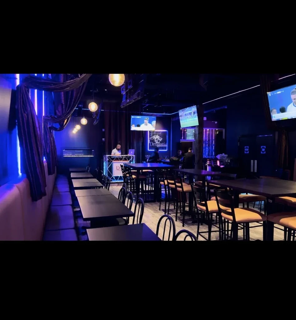 Modern lounge bar with a DJ, blue neon lighting, and sports TVs.