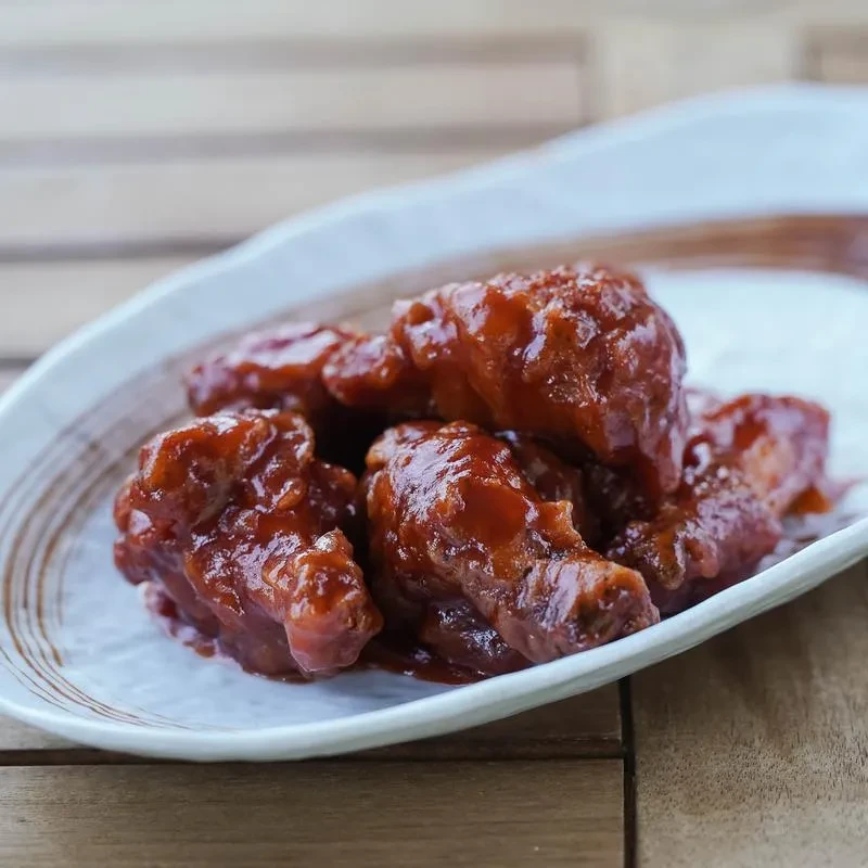 Glossy reddish-brown chicken wings piled on an off-white ceramic plate.