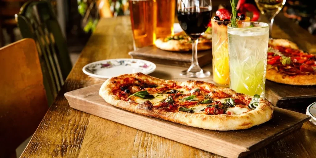 Two oblong pizzas, beers, wine, and cocktails on a rustic table.