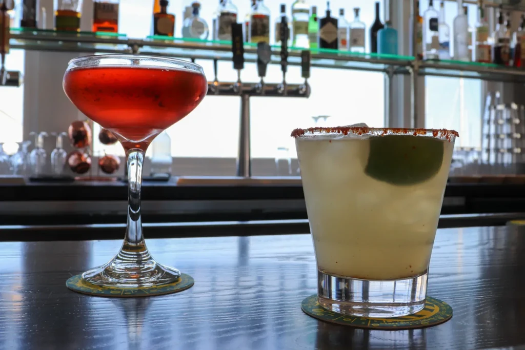 Two cocktails on a bar, a red drink and a margarita.