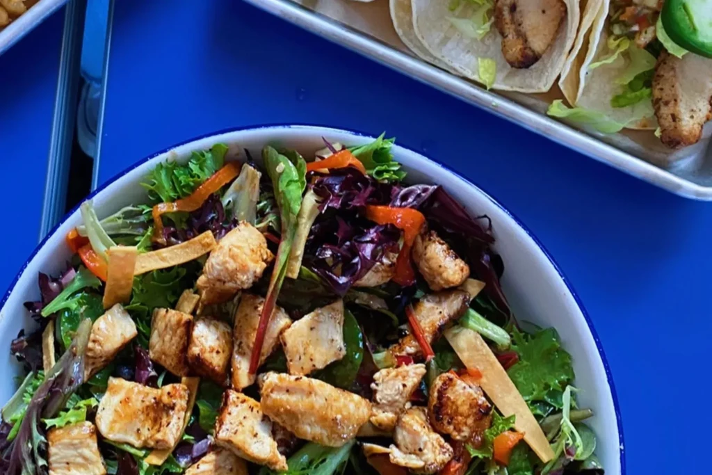 A bowl of chicken salad with a plate of tacos in the background.