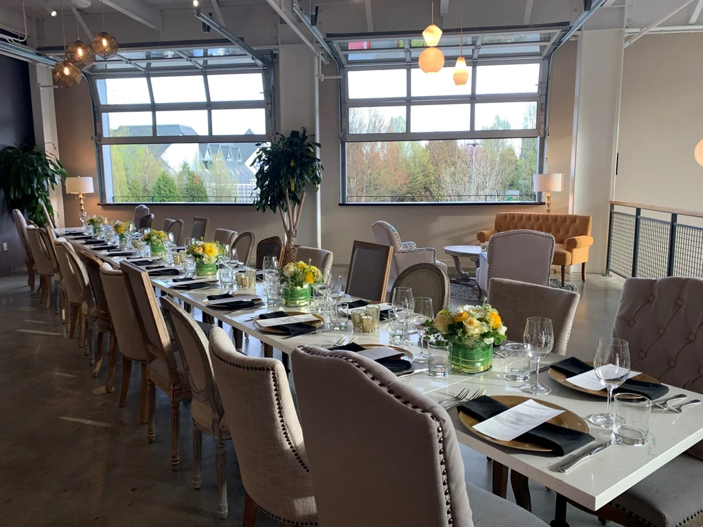 Brightly lit, long table set with gold chargers and floral centerpieces.