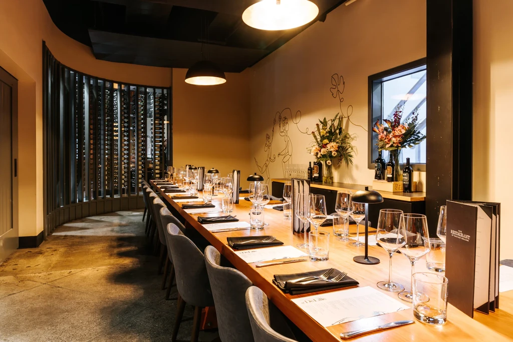 Long dining table set for dinner in a modern room with wine display.