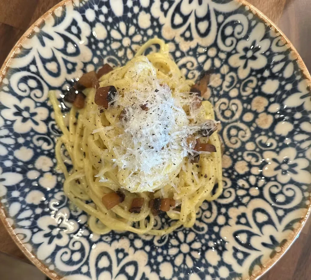 Close-up of pasta with cheese, bacon, and pepper on a patterned plate.