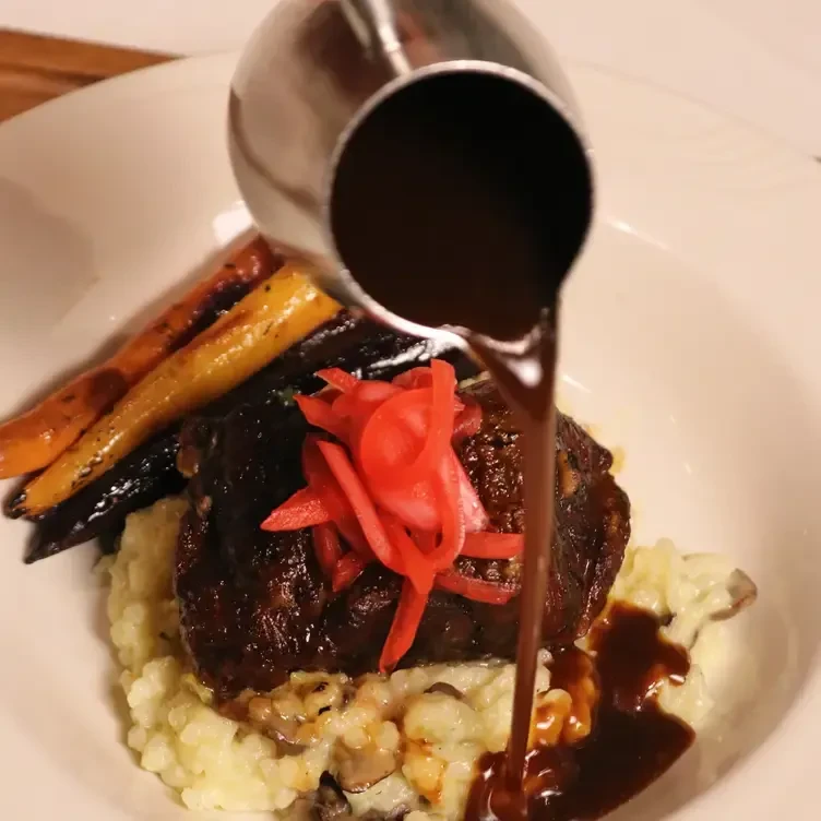 Sauce poured from a metal pitcher onto a meal of meat, rice, and carrots.