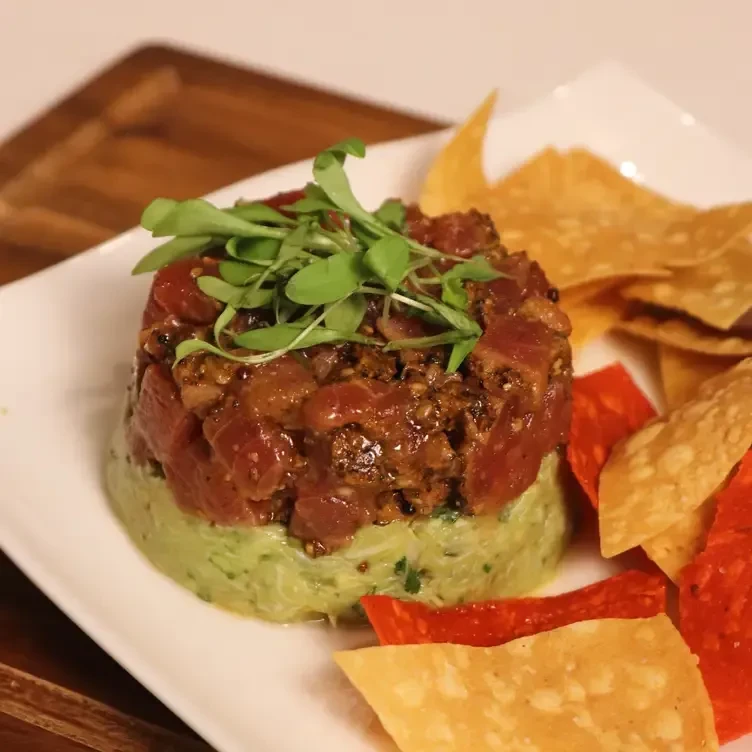 Tuna tartare with avocado and tortilla chips on a white plate.