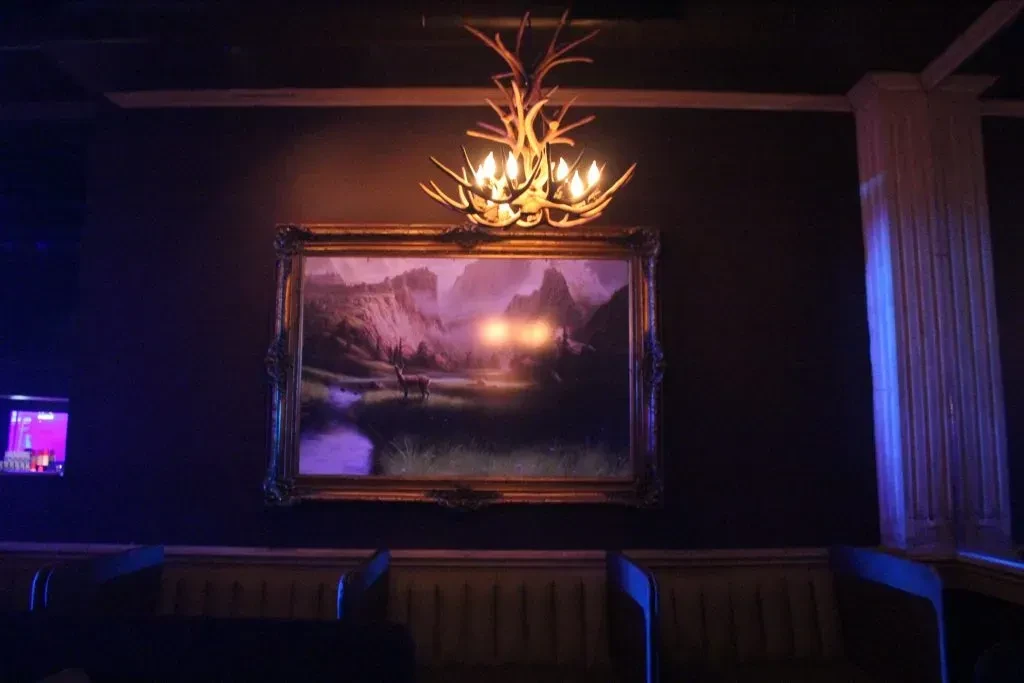 Antler chandelier above a lit deer landscape painting.