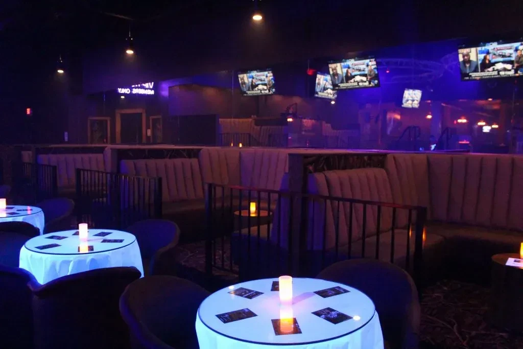 Dark, modern lounge with purple and blue lighting, booths, and tables.